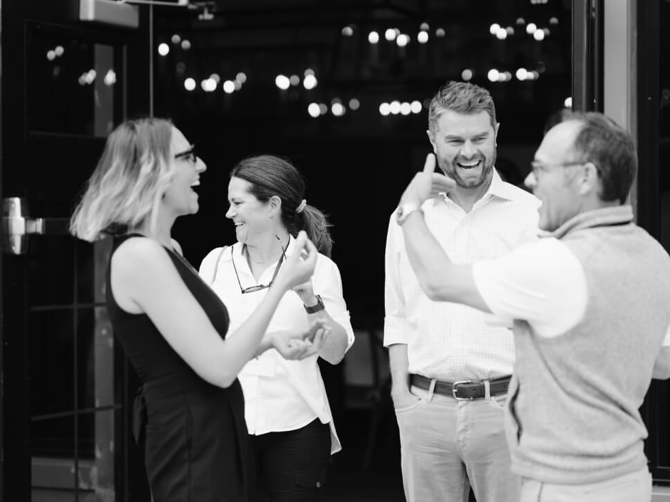 Two men and two women standing outside having a lively conversation, gesturing and smiling.